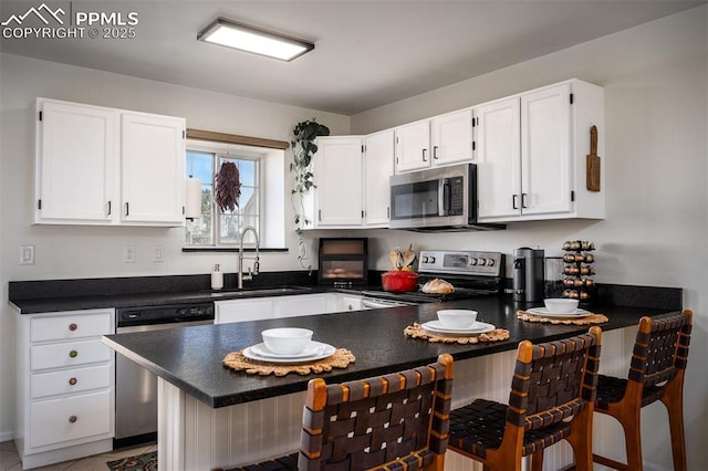 kitchen featuring stainless steel appliances, dark countertops, white cabinetry, and a kitchen bar