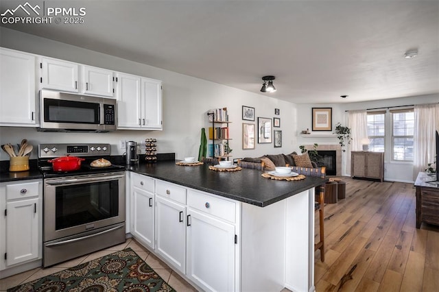 kitchen with open floor plan, a peninsula, appliances with stainless steel finishes, and dark countertops