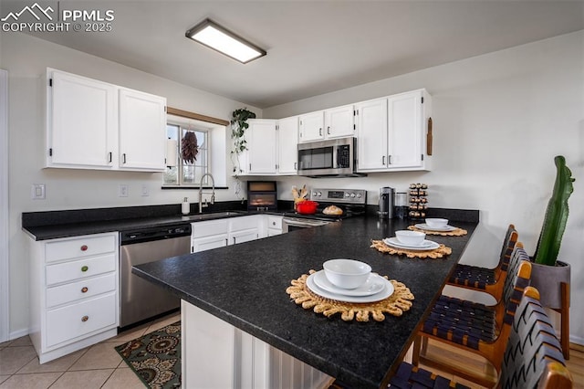 kitchen featuring dark countertops, appliances with stainless steel finishes, white cabinets, a peninsula, and a kitchen breakfast bar