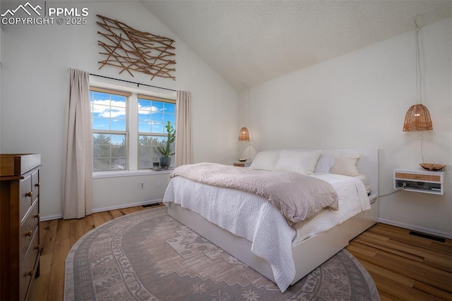 bedroom featuring baseboards, visible vents, vaulted ceiling, and wood finished floors