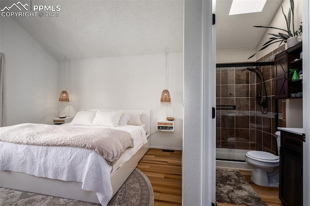 bedroom with lofted ceiling with skylight, a textured ceiling, and wood finished floors