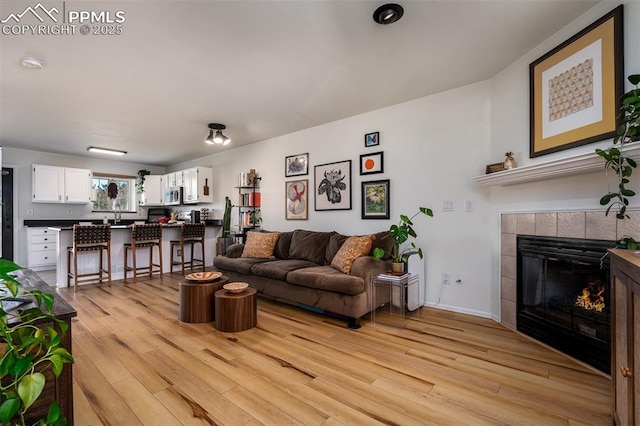 living room with light wood finished floors, a tile fireplace, and baseboards