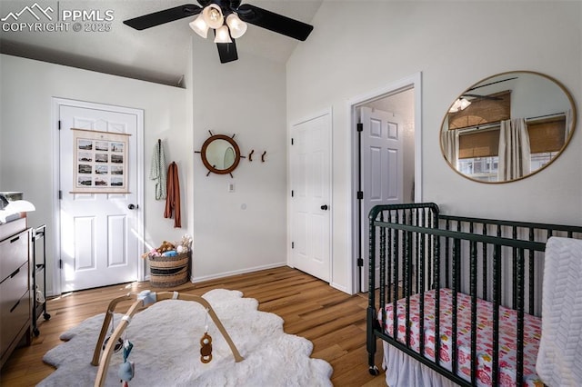 bedroom with a nursery area, a ceiling fan, vaulted ceiling, and wood finished floors