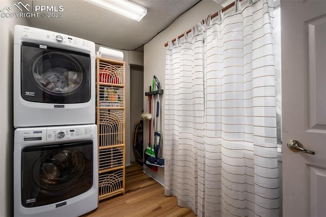 clothes washing area featuring stacked washer and dryer, a textured ceiling, and wood finished floors