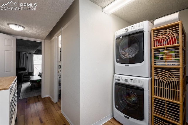 laundry area featuring a textured ceiling, laundry area, wood finished floors, baseboards, and stacked washing maching and dryer