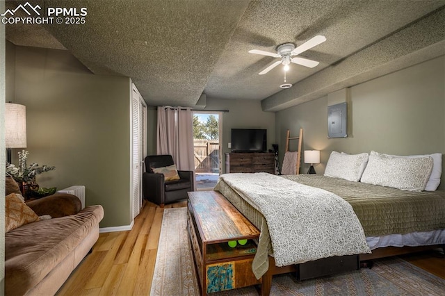 bedroom featuring a textured ceiling, wood finished floors, access to exterior, baseboards, and electric panel