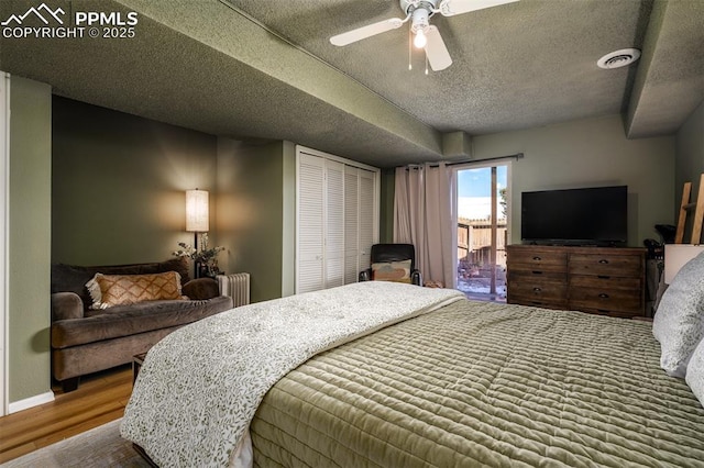 bedroom featuring visible vents, radiator heating unit, a textured ceiling, wood finished floors, and baseboards