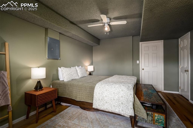 bedroom with a textured ceiling, electric panel, baseboards, and wood finished floors