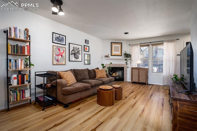 living room with light wood-style floors, a tile fireplace, and baseboards