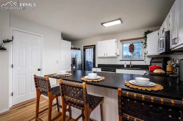 kitchen with dark countertops, stainless steel appliances, light wood-type flooring, white cabinetry, and a sink