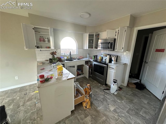 kitchen featuring stainless steel appliances, a sink, white cabinets, light countertops, and decorative backsplash