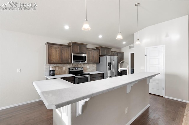 kitchen featuring an island with sink, pendant lighting, stainless steel appliances, and a kitchen breakfast bar