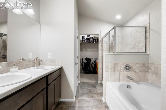 bathroom featuring a spacious closet, double vanity, a sink, and a bath