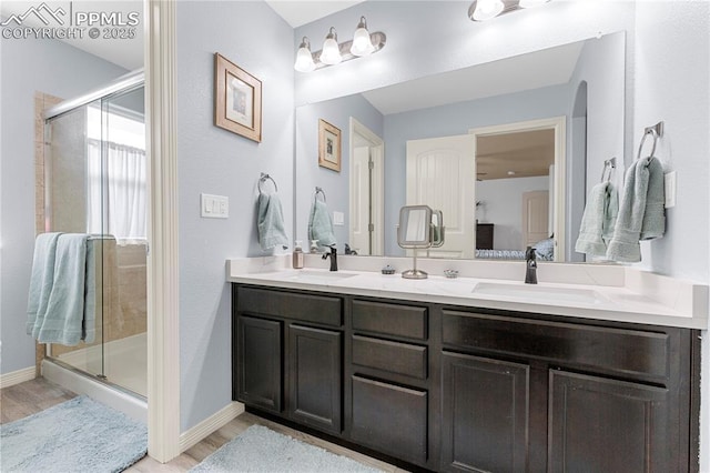 ensuite bathroom with a stall shower, a sink, and wood finished floors