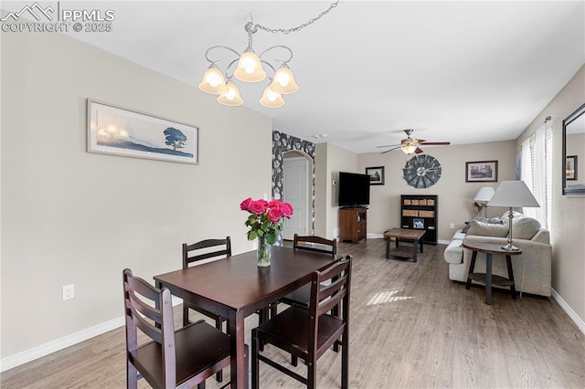 dining room with arched walkways, ceiling fan with notable chandelier, wood finished floors, and baseboards