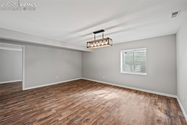 unfurnished room featuring dark wood finished floors, visible vents, and baseboards