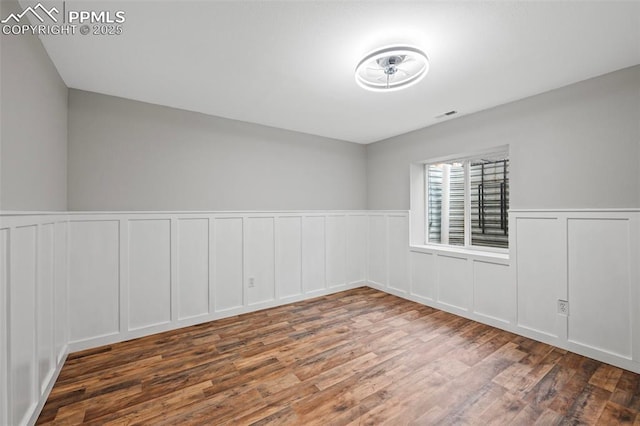 spare room featuring wainscoting, visible vents, a decorative wall, and wood finished floors