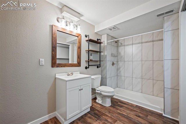 full bath featuring toilet, wood finished floors, vanity, visible vents, and a tile shower