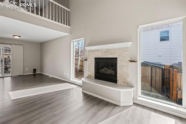 unfurnished living room featuring a high ceiling, a fireplace, baseboards, and wood finished floors