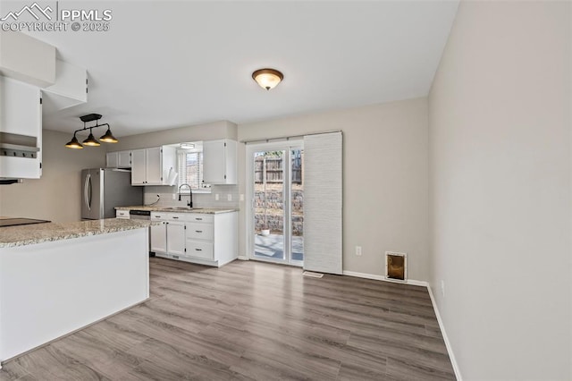 kitchen featuring a sink, wood finished floors, baseboards, white cabinets, and freestanding refrigerator