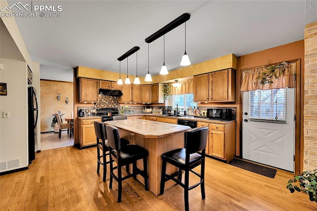 kitchen featuring under cabinet range hood, a kitchen island, a kitchen breakfast bar, light wood-type flooring, and black appliances