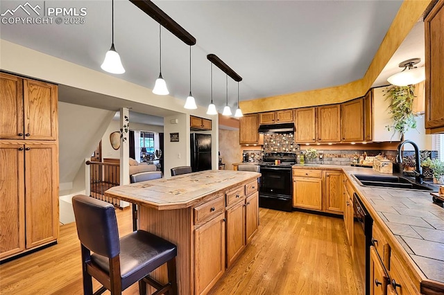 kitchen with tile countertops, black appliances, a sink, and under cabinet range hood