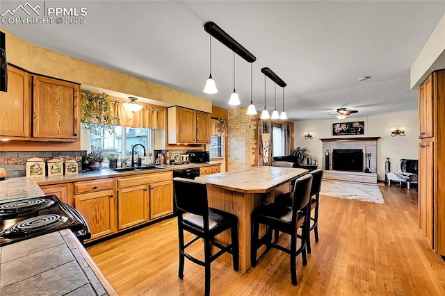 kitchen with tile countertops, light wood-type flooring, a fireplace, and a sink