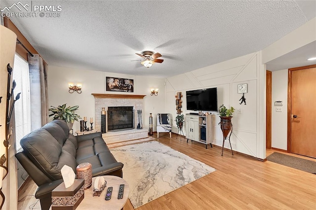 living area with a brick fireplace, ceiling fan, a textured ceiling, and wood finished floors