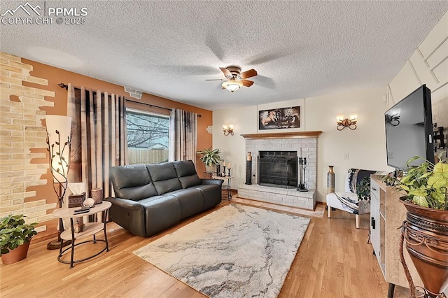 living area with a ceiling fan, a brick fireplace, a textured ceiling, and light wood finished floors