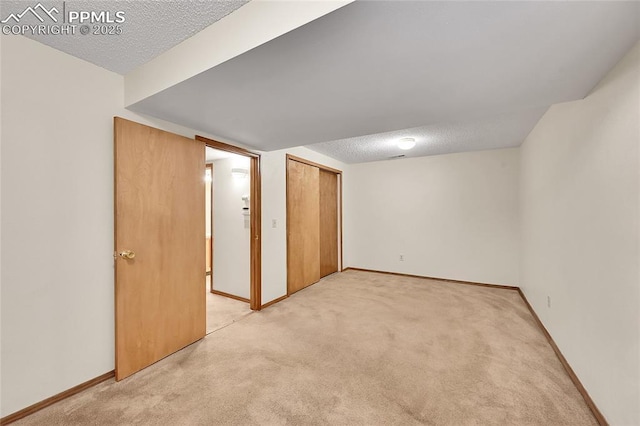 spare room featuring light carpet, a textured ceiling, and baseboards