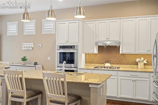 kitchen with tasteful backsplash, appliances with stainless steel finishes, white cabinets, a sink, and under cabinet range hood