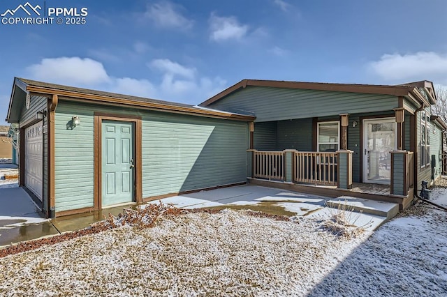 snow covered house with covered porch and a garage