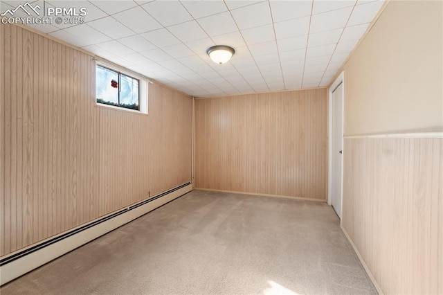 basement featuring a baseboard heating unit, light colored carpet, and wooden walls