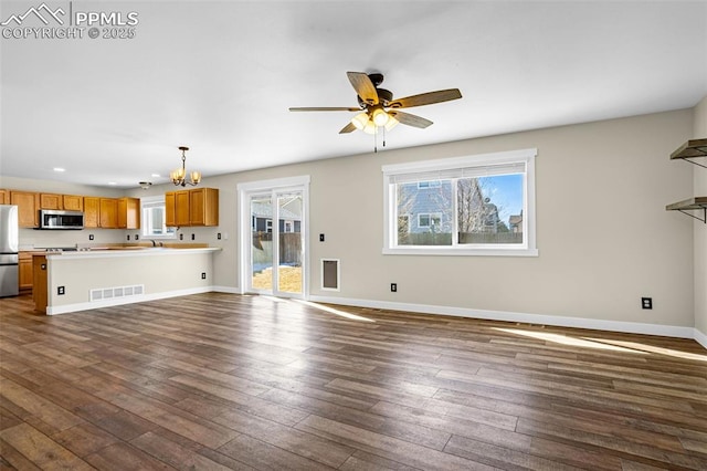 unfurnished living room with ceiling fan with notable chandelier, dark wood finished floors, visible vents, and baseboards