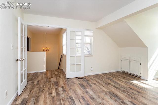 additional living space with lofted ceiling, french doors, a notable chandelier, and wood finished floors