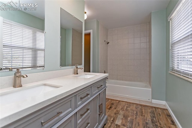 bathroom with wood finished floors, a sink, baseboards,  shower combination, and double vanity