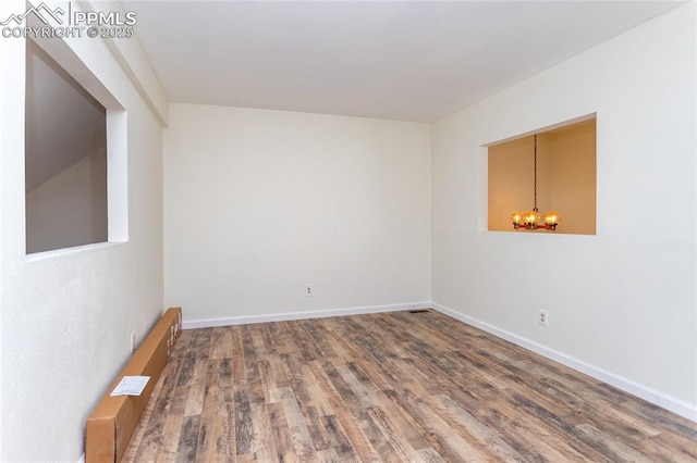 unfurnished room with a chandelier, visible vents, baseboards, and wood finished floors