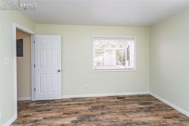 empty room with electric panel, visible vents, baseboards, and wood finished floors