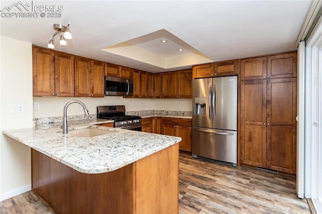 kitchen with a peninsula, brown cabinetry, stainless steel appliances, and a sink