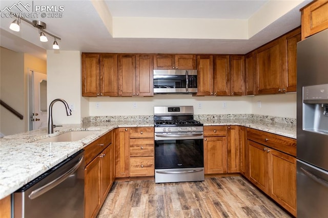 kitchen featuring light wood finished floors, light stone counters, appliances with stainless steel finishes, brown cabinets, and a sink