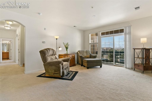 sitting room featuring arched walkways, light carpet, visible vents, and baseboards