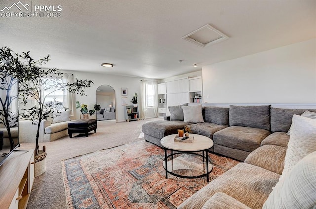 carpeted living area featuring plenty of natural light, a textured ceiling, arched walkways, and attic access