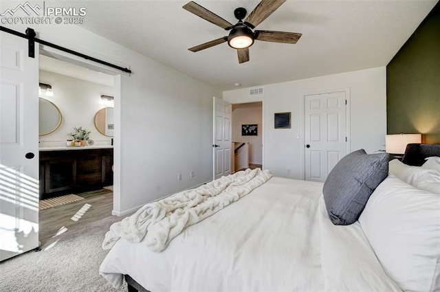 bedroom featuring visible vents, a barn door, carpet flooring, ceiling fan, and ensuite bath