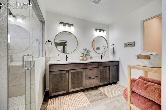 full bath featuring wood finished floors, a sink, visible vents, and a shower stall