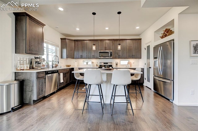 kitchen with a kitchen island, appliances with stainless steel finishes, a kitchen breakfast bar, dark wood-style flooring, and dark brown cabinets