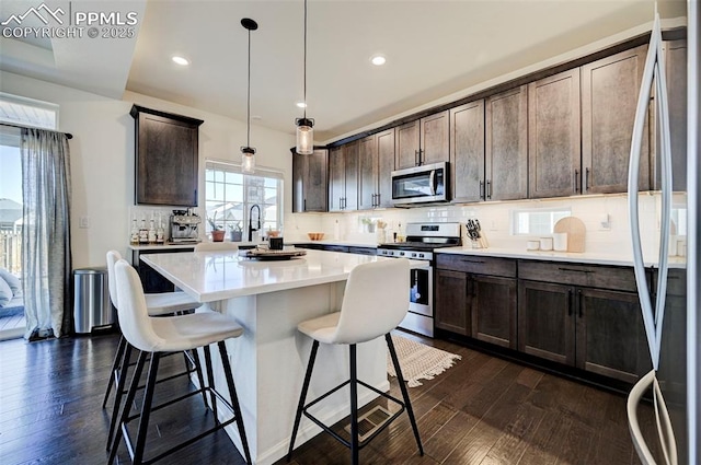 kitchen with dark brown cabinetry, dark wood-style floors, appliances with stainless steel finishes, and a breakfast bar area