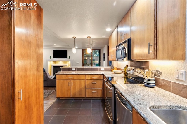 kitchen featuring stainless steel appliances, open floor plan, brown cabinetry, and a peninsula