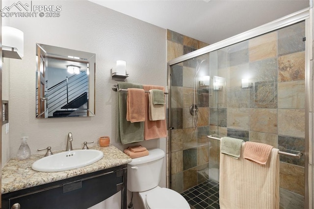 bathroom with toilet, a textured wall, a shower stall, and vanity