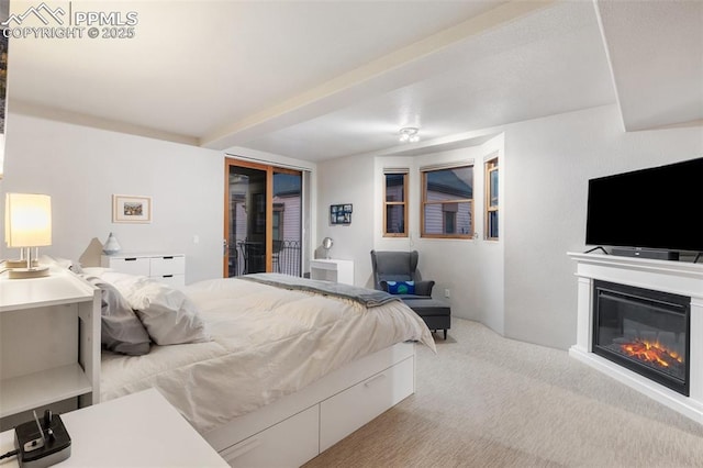 bedroom featuring access to exterior, a glass covered fireplace, and light colored carpet