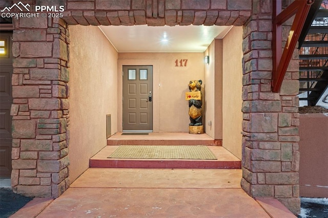 view of exterior entry featuring stone siding and stucco siding